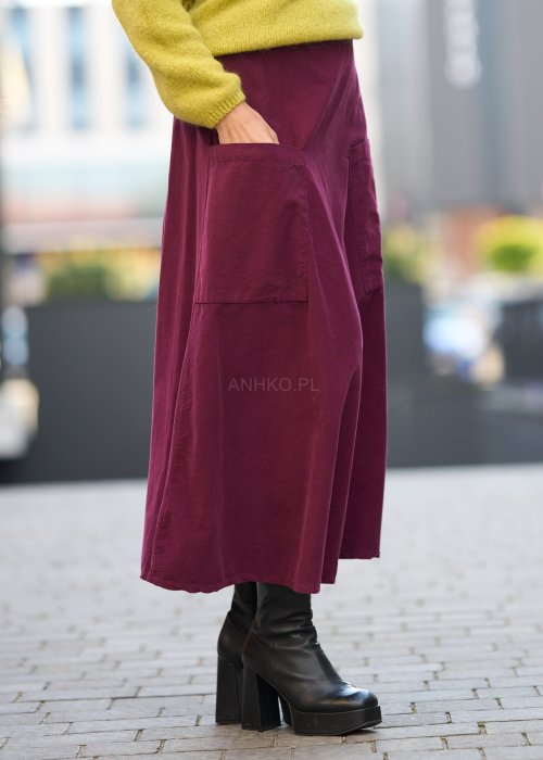 Śliwkowa spódnica sztruksowa midi z naszywanymi kieszeniami i elastycznym pasem, zestawiona z limonkowym swetrem i czarnymi botkami w miejskiej stylizacji.