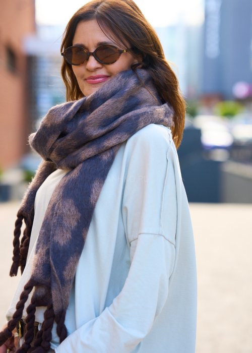 Miękki szal z motywem panterki, zakończony grubymi, plecionymi frędzlami.