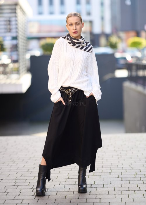 Czarna spódnica dzianinowa o asymetrycznym dole i elastycznym pasie z ozdobnym paskiem. Model pokazany w stylizacji z jasnym swetrem i czarnymi botkami na obcasie.