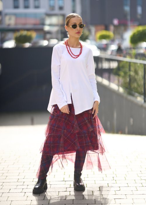 Biała bluzka damska z długim rękawem i wycięciem, w stylizacji z czerwoną spódnicą tiulową.