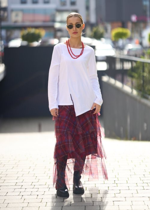 Biała bluzka damska z długim rękawem i wycięciem, w stylizacji z czerwoną spódnicą tiulową.