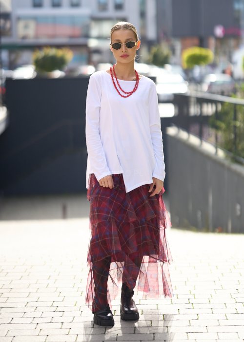 Biała bluzka damska z długim rękawem i wycięciem, w stylizacji z czerwoną spódnicą tiulową.