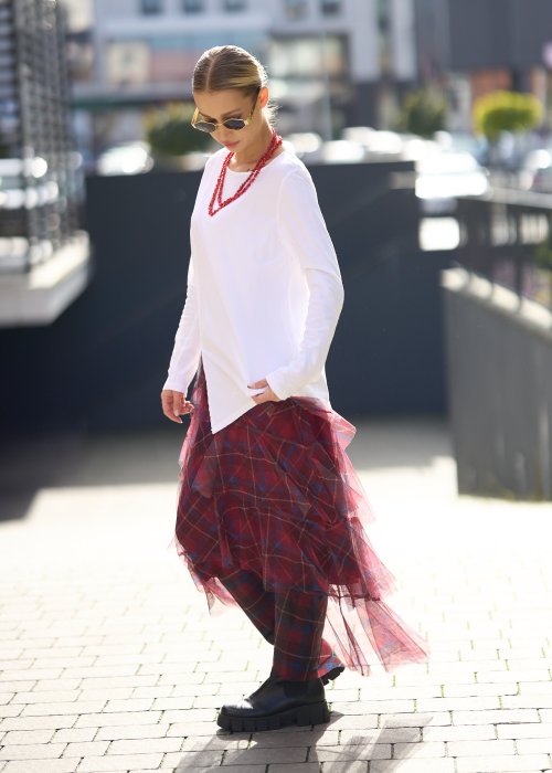 Biała bluzka damska z długim rękawem i wycięciem, w stylizacji z czerwoną spódnicą tiulową.