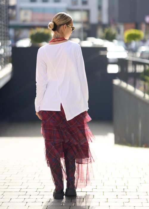 Biała bluzka damska z długim rękawem i wycięciem, w stylizacji z czerwoną spódnicą tiulową.