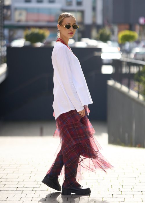 Biała bluzka damska z długim rękawem i wycięciem, w stylizacji z czerwoną spódnicą tiulową.