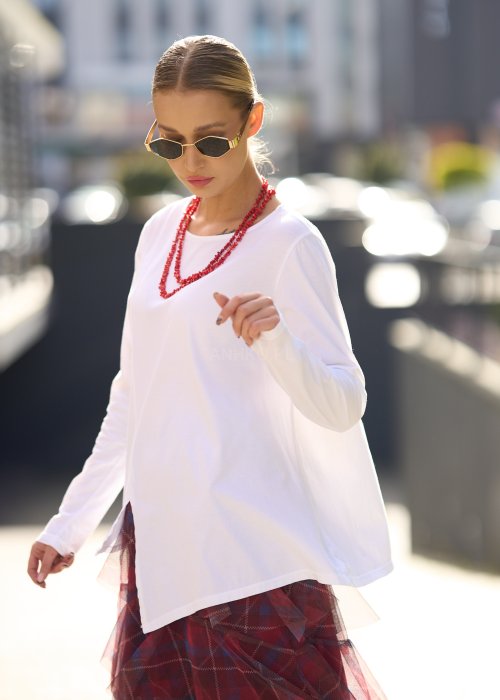 Biała bluzka damska z długim rękawem i wycięciem, w stylizacji z czerwoną spódnicą tiulową.