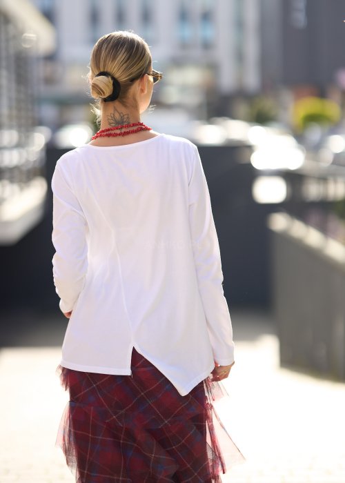 Biała bluzka damska z długim rękawem i wycięciem, w stylizacji z czerwoną spódnicą tiulową.