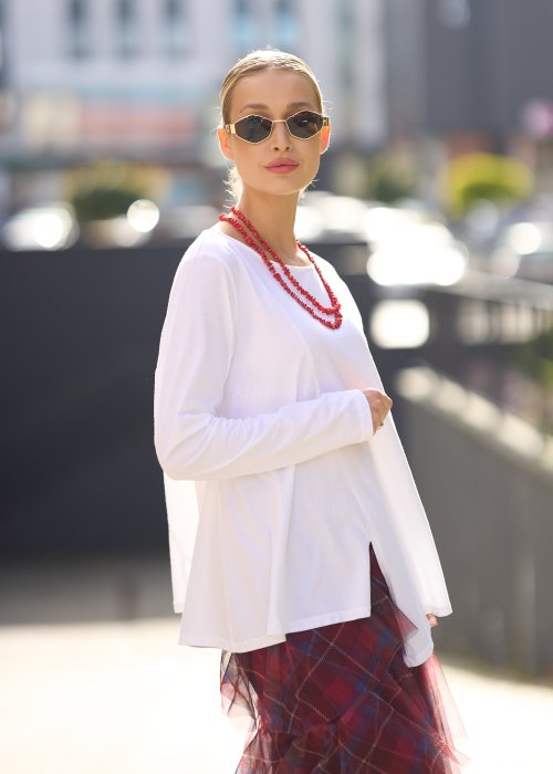 Biała bluzka damska z długim rękawem i wycięciem, w stylizacji z czerwoną spódnicą tiulową.