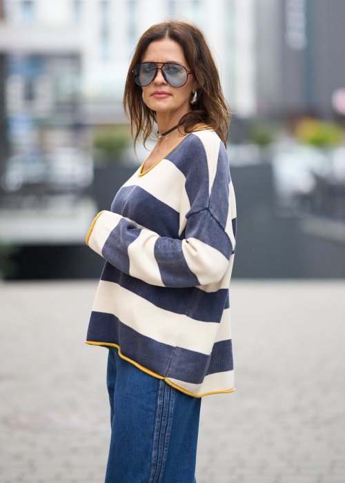 Kobieta w oversize swetrze w szerokie granatowo-kremowe pasy z żółtą lamówką, luźna stylizacja z jeansami, moda damska casual