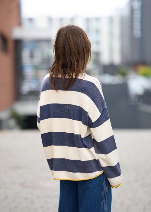 Kobieta w oversize swetrze w szerokie granatowo-kremowe pasy z żółtą lamówką, luźna stylizacja z jeansami, moda damska casual