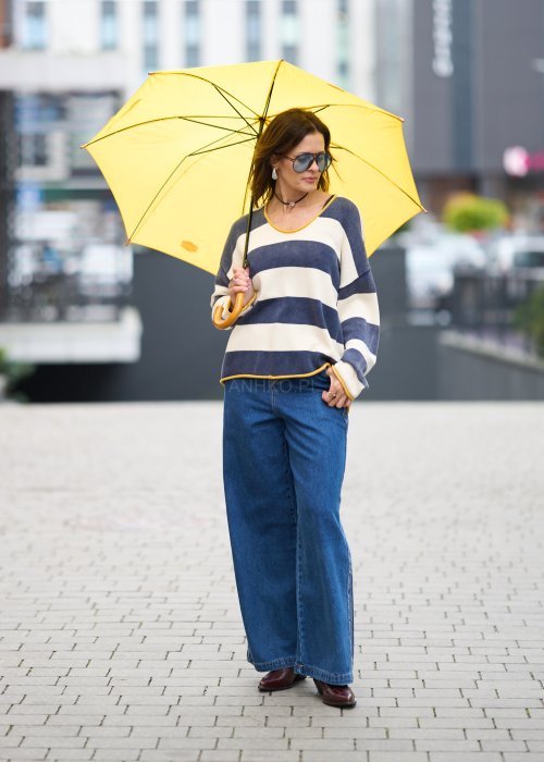 Kobieta w oversize swetrze w szerokie granatowo-kremowe pasy z żółtą lamówką, luźna stylizacja z jeansami, moda damska casual