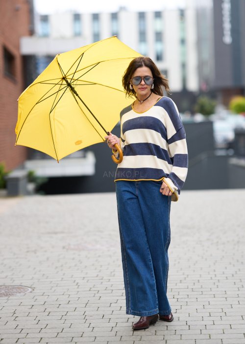 Kobieta w oversize swetrze w szerokie granatowo-kremowe pasy z żółtą lamówką, luźna stylizacja z jeansami, moda damska casual