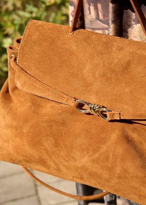 Karmelowa-torebka-z-zamszu-o-miekkiej-strukturze,-z-klapa-i-metalowym-zapieciem,-trzymana-w-dloni-kobiety-w-jesiennej-stylizacji-z-dluga,-wzorzysta-spodnica.-3.jpg
