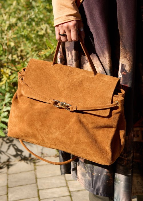 Karmelowa-torebka-z-zamszu-o-miekkiej-strukturze,-z-klapa-i-metalowym-zapieciem,-trzymana-w-dloni-kobiety-w-jesiennej-stylizacji-z-dluga,-wzorzysta-spodnica..jpg