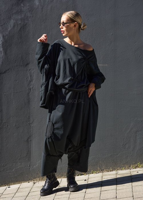 Czarne spodnie damskie oversize z obniżonym krokiem i ozdobnymi aplikacjami, zestawione z botkami i luźną bluzą w nowoczesnej stylizacji streetwear.