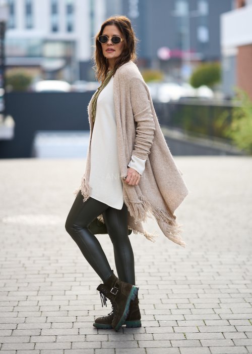 Beżowa narzutka z miękkiej dzianiny, luźny krój oversize i długie frędzle, styl boho w modzie damskiej