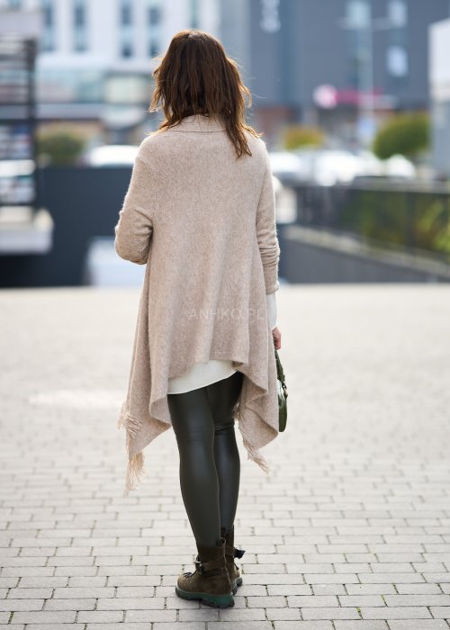 Beżowa narzutka z miękkiej dzianiny, luźny krój oversize i długie frędzle, styl boho w modzie damskiej