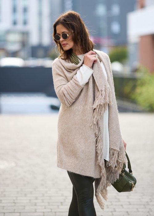Beżowa narzutka z miękkiej dzianiny, luźny krój oversize i długie frędzle, styl boho w modzie damskiej