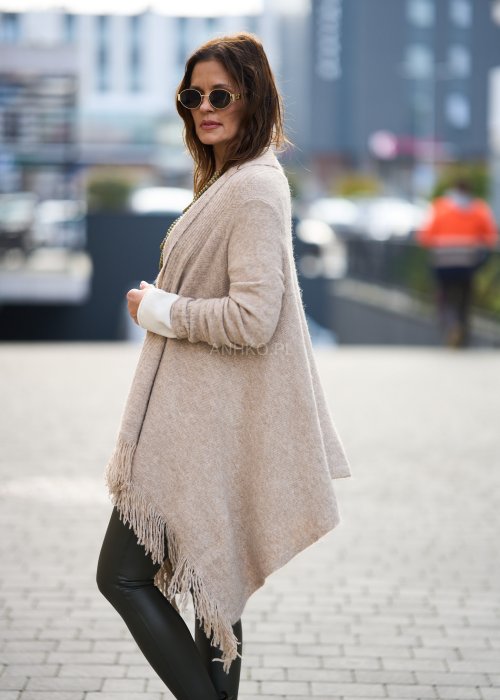 Beżowa narzutka z miękkiej dzianiny, luźny krój oversize i długie frędzle, styl boho w modzie damskiej
