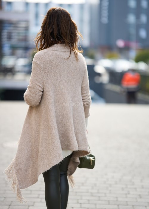 Beżowa narzutka z miękkiej dzianiny, luźny krój oversize i długie frędzle, styl boho w modzie damskiej