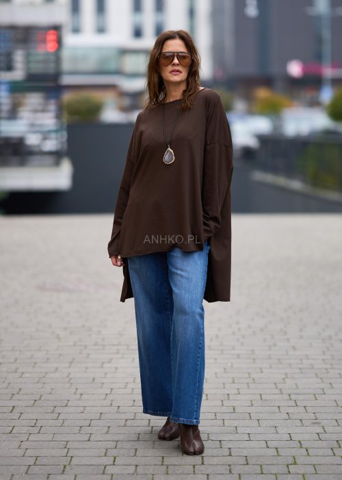 Czekoladowa bluzka oversize z dłuższym tyłem i długim rękawem, zestawiona z niebieskimi jeansami w swobodnej, miejskiej stylizacji.