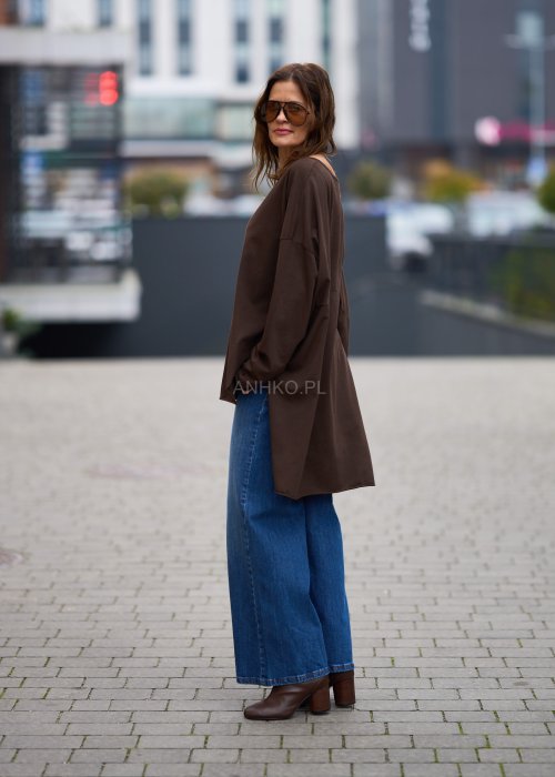 Czekoladowa bluzka oversize z dłuższym tyłem i długim rękawem, zestawiona z niebieskimi jeansami w swobodnej, miejskiej stylizacji.