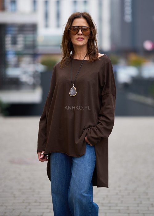Czekoladowa bluzka oversize z dłuższym tyłem i długim rękawem, zestawiona z niebieskimi jeansami w swobodnej, miejskiej stylizacji.
