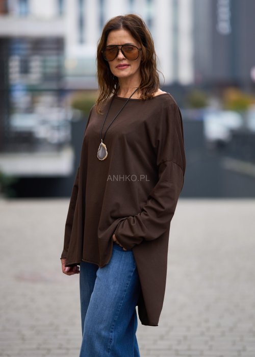 Czekoladowa bluzka oversize z dłuższym tyłem i długim rękawem, zestawiona z niebieskimi jeansami w swobodnej, miejskiej stylizacji.