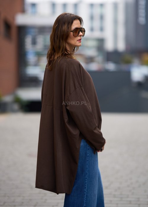 Czekoladowa bluzka oversize z dłuższym tyłem i długim rękawem, zestawiona z niebieskimi jeansami w swobodnej, miejskiej stylizacji.