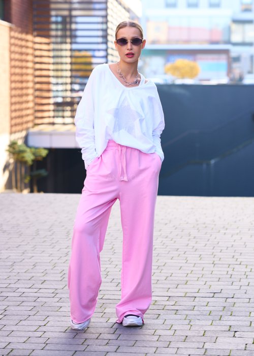 Różowe spodnie dresowe damskie z elastyczną talią i sznurkiem, o luźnym kroju i długich nogawkach, stylizowane w miejskim casualowym looku ze sneakersami.