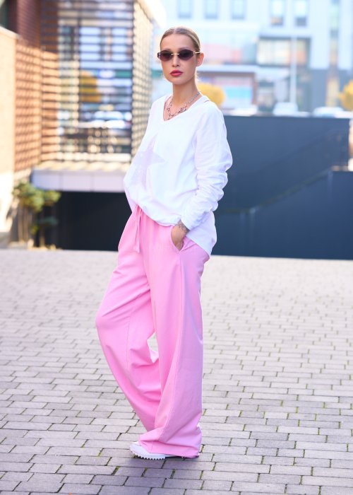 Różowe spodnie dresowe damskie z elastyczną talią i sznurkiem, o luźnym kroju i długich nogawkach, stylizowane w miejskim casualowym looku ze sneakersami.