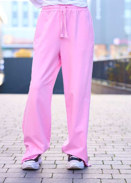 Różowe spodnie dresowe damskie z elastyczną talią i sznurkiem, o luźnym kroju i długich nogawkach, stylizowane w miejskim casualowym looku ze sneakersami.
