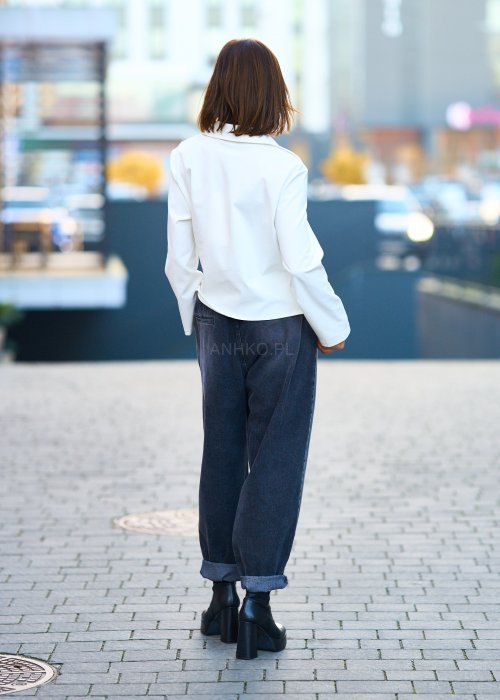 Biała koszula damska z asymetrycznym wiązaniem i klasycznym kołnierzem. Stylizacja z ciemnymi spodniami i biżuterią w eleganckim, miejskim stylu.