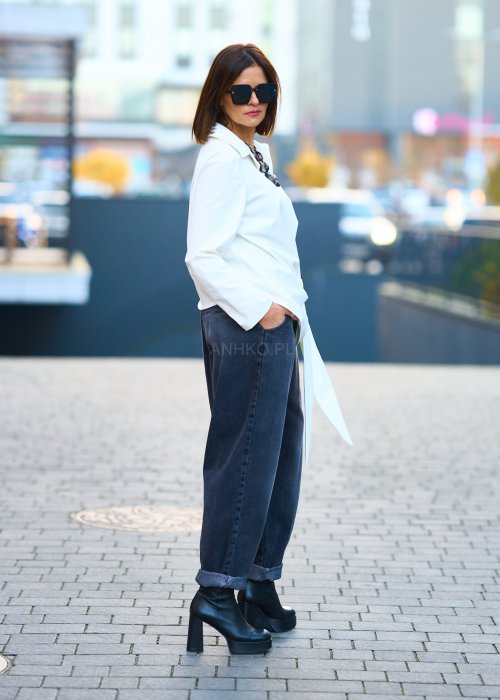 Biała koszula damska z asymetrycznym wiązaniem i klasycznym kołnierzem. Stylizacja z ciemnymi spodniami i biżuterią w eleganckim, miejskim stylu.