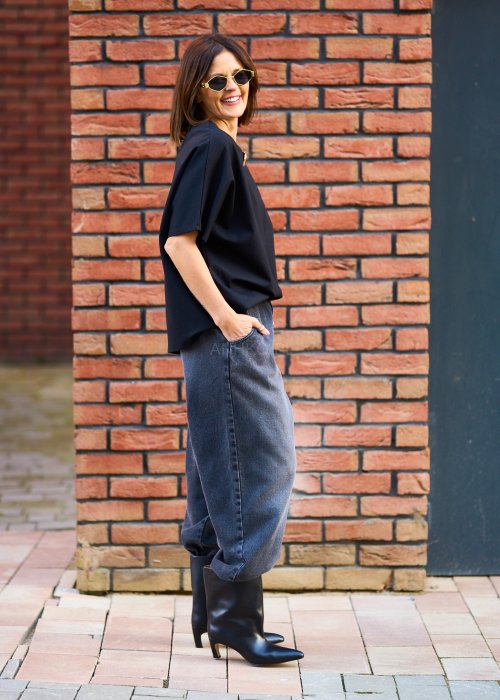 Antracytowe jeansy damskie o luźnym kroju z podwiniętymi nogawkami, stylizowane z czarnym topem i botkami na obcasie w miejskim looku.