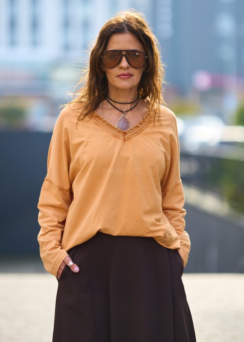 Kobieta w pomarańczowej bluzce z dekoltem w serek i brązowej spódnicy, casualowa stylizacja w ciepłych jesiennych kolorach