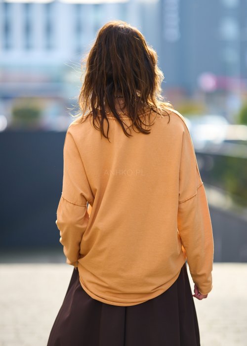 Kobieta w pomarańczowej bluzce z dekoltem w serek i brązowej spódnicy, casualowa stylizacja w ciepłych jesiennych kolorach