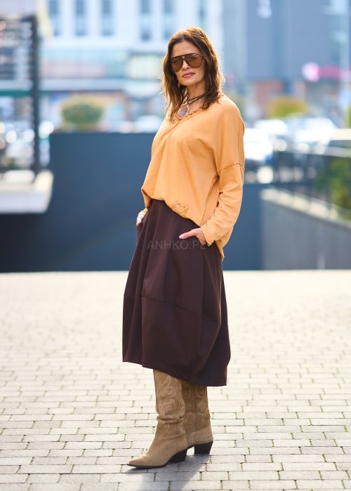 Kobieta w pomarańczowej bluzce z dekoltem w serek i brązowej spódnicy, casualowa stylizacja w ciepłych jesiennych kolorach