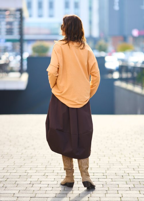 Kobieta w pomarańczowej bluzce z dekoltem w serek i brązowej spódnicy, casualowa stylizacja w ciepłych jesiennych kolorach