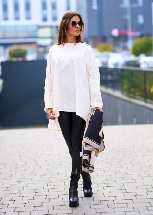 Kobieta w oversize kremowej bluzce z długim rękawem i legginsach ze skóry ekologicznej, minimalistyczna stylizacja w miejskim stylu
