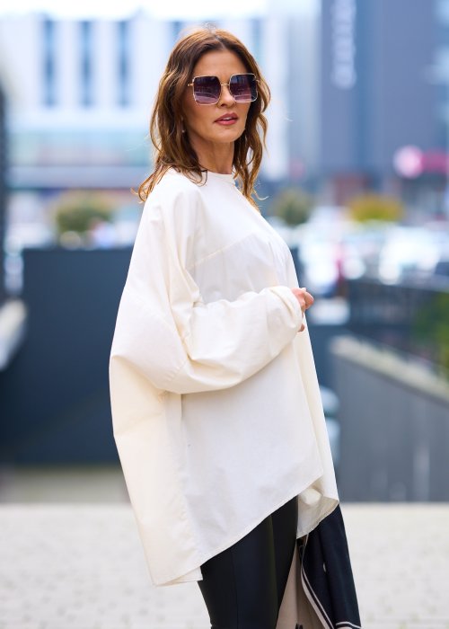 Kobieta w oversize kremowej bluzce z długim rękawem i legginsach ze skóry ekologicznej, minimalistyczna stylizacja w miejskim stylu