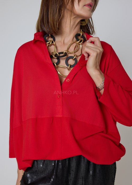 Czerwona koszula damska oversize z kołnierzykiem i przeszyciem poniżej biustu, zestawiona z czarnymi spodniami z połyskiem w eleganckiej stylizacji.