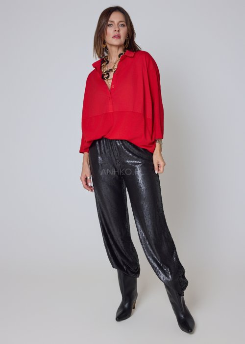Czerwona koszula damska oversize z kołnierzykiem i przeszyciem poniżej biustu, zestawiona z czarnymi spodniami z połyskiem w eleganckiej stylizacji.