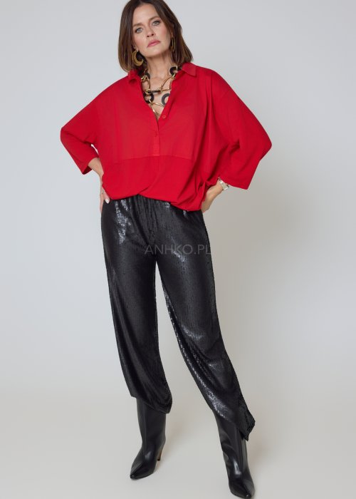 Czerwona koszula damska oversize z kołnierzykiem i przeszyciem poniżej biustu, zestawiona z czarnymi spodniami z połyskiem w eleganckiej stylizacji.