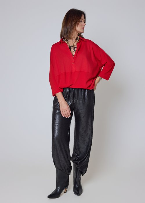 Czerwona koszula damska oversize z kołnierzykiem i przeszyciem poniżej biustu, zestawiona z czarnymi spodniami z połyskiem w eleganckiej stylizacji.