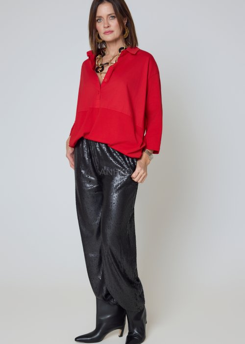 Czerwona koszula damska oversize z kołnierzykiem i przeszyciem poniżej biustu, zestawiona z czarnymi spodniami z połyskiem w eleganckiej stylizacji.