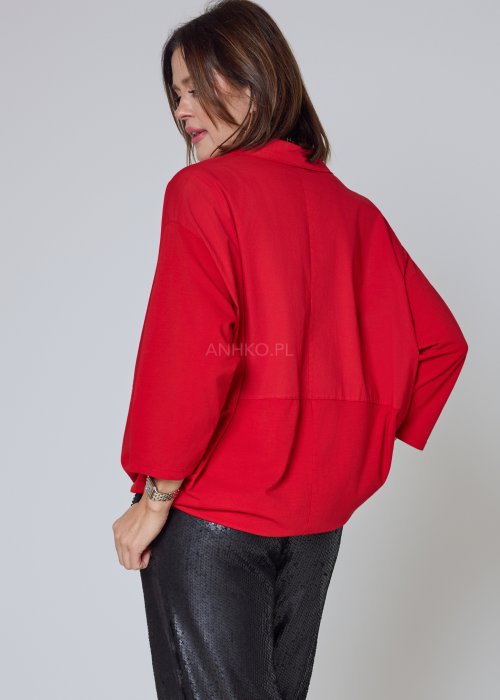 Czerwona koszula damska oversize z kołnierzykiem i przeszyciem poniżej biustu, zestawiona z czarnymi spodniami z połyskiem w eleganckiej stylizacji.