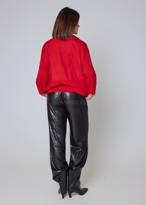 Czerwona koszula damska oversize z kołnierzykiem i przeszyciem poniżej biustu, zestawiona z czarnymi spodniami z połyskiem w eleganckiej stylizacji.