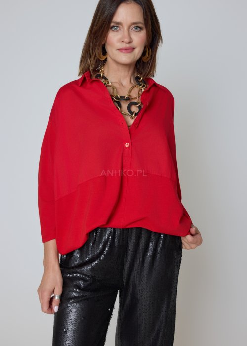 Czerwona koszula damska oversize z kołnierzykiem i przeszyciem poniżej biustu, zestawiona z czarnymi spodniami z połyskiem w eleganckiej stylizacji.