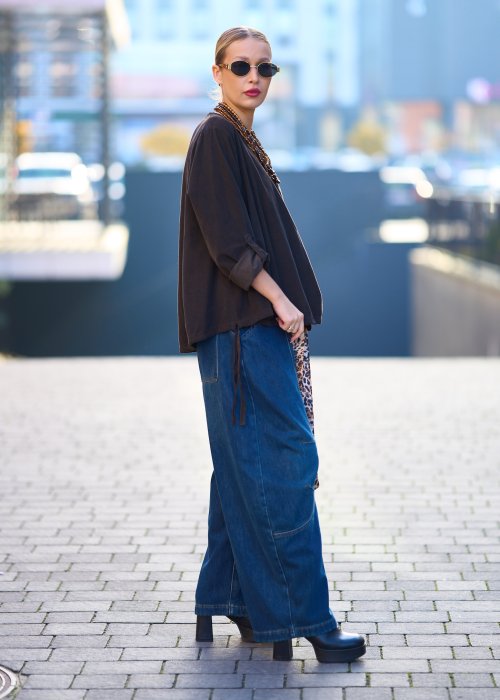 Bluzka oversize w kolorze głębokiego brązu z długim rękawem i regulowanym dołem na troczki, zestawiona z jeansami w miejskiej stylizacji